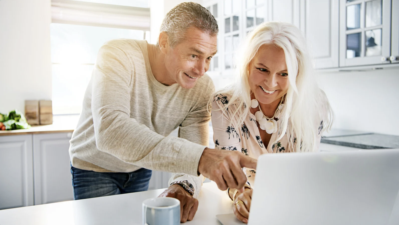 A man and woman sit together, enjoying coffee while viewing something on a laptop screen.