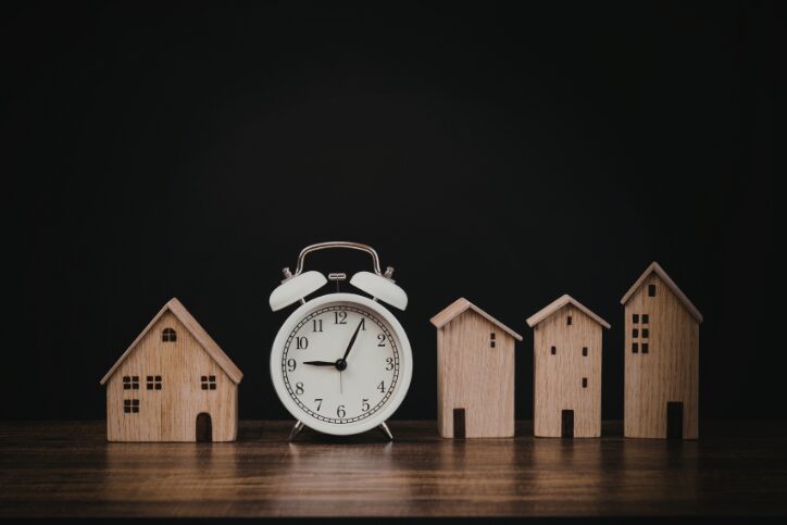 Alarm clock lined up with house figurines in a dark room.